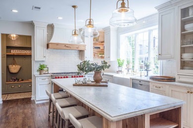 Example of a farmhouse medium tone wood floor and brown floor kitchen design in DC Metro with a farmhouse sink, beaded inset cabinets, white cabinets, quartzite countertops, beige backsplash, subway tile backsplash, stainless steel appliances and beige countertops