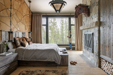 Bedroom - large rustic master light wood floor and brown floor bedroom idea in Other with beige walls, a standard fireplace and a stone fireplace