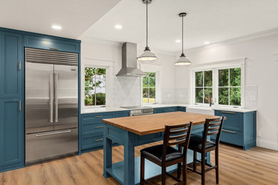 Example of a mid-sized cottage vinyl floor and brown floor kitchen design in Portland with a farmhouse sink, shaker cabinets, blue cabinets, quartz countertops, white backsplash, ceramic backsplash, stainless steel appliances, an island and white countertops