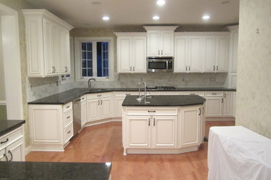 Enclosed kitchen - large traditional l-shaped light wood floor and brown floor enclosed kitchen idea in Other with an undermount sink, raised-panel cabinets, white cabinets, granite countertops, gray backsplash, porcelain backsplash, stainless steel appliances, an island and gray countertops