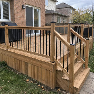 Cedar deck with black aluminum spindles in a cedar railing frame and stairs to a
