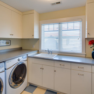 ミネアポリスの中サイズのトラディショナルスタイルのおしゃれな洗濯室 (ドロップインシンク、フラットパネル扉のキャビネット、白いキャビネット、ラミネートカウンター、黄色い壁、リノリウムの床、左右配置の洗濯機・乾燥機) の写真