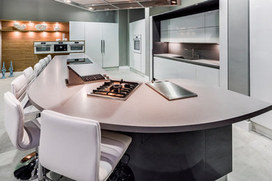This is an example of an expansive contemporary single-wall eat-in kitchen in San Francisco with a single-bowl sink, flat-panel cabinets, white cabinets, quartz benchtops, grey splashback, white appliances, porcelain floors and with island.