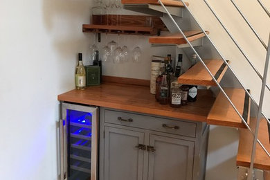 Small trendy single-wall home bar photo in New York with no sink, gray cabinets, wood countertops and white backsplash