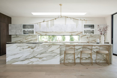 Huge trendy l-shaped light wood floor and brown floor kitchen photo in Los Angeles with a drop-in sink, flat-panel cabinets, white backsplash, stone slab backsplash, stainless steel appliances, an island and white countertops
