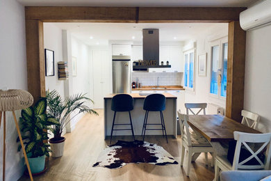 Imagen de cocina pequeña abierta con fregadero bajoencimera, armarios con paneles lisos, puertas de armario blancas, encimera de madera, salpicadero blanco, salpicadero de azulejos de cerámica, electrodomésticos de acero inoxidable, suelo de madera en tonos medios, una isla, suelo marrón y encimeras marrones