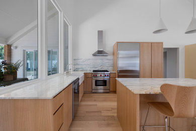 Example of a large l-shaped light wood floor, brown floor and vaulted ceiling open concept kitchen design in Austin with a farmhouse sink, flat-panel cabinets, light wood cabinets, marble countertops, multicolored backsplash, granite backsplash, stainless steel appliances, an island and white countertops