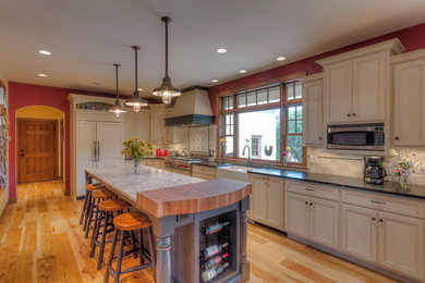 Eat-in kitchen - rustic l-shaped medium tone wood floor eat-in kitchen idea in Other with a farmhouse sink, raised-panel cabinets, white cabinets, granite countertops, white backsplash, ceramic backsplash, an island and paneled appliances