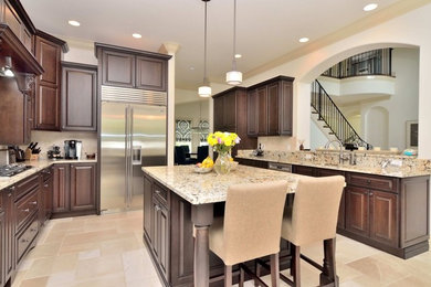 Large elegant u-shaped travertine floor and beige floor eat-in kitchen photo in Tampa with an undermount sink, raised-panel cabinets, medium tone wood cabinets, granite countertops, multicolored backsplash, mosaic tile backsplash, stainless steel appliances and an island