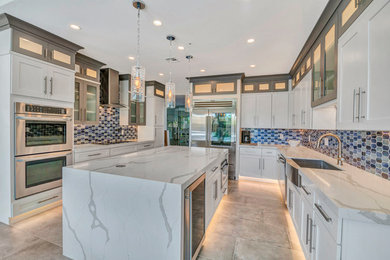 Large beach style u-shaped eat-in kitchen in Phoenix with a farmhouse sink, shaker cabinets, white cabinets, quartz benchtops, blue splashback, glass tile splashback, stainless steel appliances, porcelain floors, with island, grey floor and white benchtop.