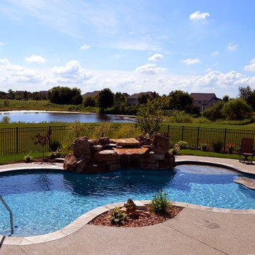 Free form pool with stone table, sun shelf, water feature, and outdoor kitchen,