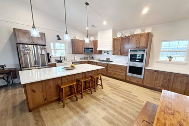 Eat-in kitchen - mid-sized rustic l-shaped eat-in kitchen idea in Other with a farmhouse sink, shaker cabinets, quartz countertops, white backsplash, stainless steel appliances, an island and white countertops