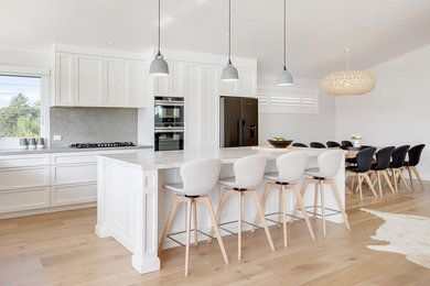 Design ideas for a large beach style l-shaped eat-in kitchen in Sydney with a double-bowl sink, shaker cabinets, white cabinets, quartz benchtops, grey splashback, porcelain splashback, stainless steel appliances, bamboo floors, with island and grey benchtop.