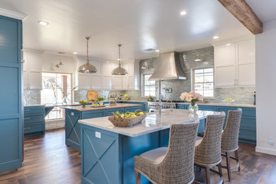 Inspiration for a large country u-shaped kitchen in Oklahoma City with a farmhouse sink, shaker cabinets, blue cabinets, quartzite benchtops, multi-coloured splashback, glass tile splashback, stainless steel appliances, medium hardwood floors, multiple islands, white benchtop and brown floor.