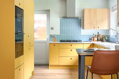 Photo of a medium sized retro u-shaped open plan kitchen in Other with an integrated sink, flat-panel cabinets, yellow cabinets, quartz worktops, blue splashback, ceramic splashback, black appliances, vinyl flooring, a breakfast bar, brown floors and white worktops.
