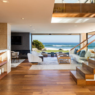 Exempel på ett mycket stort modernt allrum med öppen planlösning, med beige väggar, ljust trägolv, en bred öppen spis, en spiselkrans i betong, en väggmonterad TV och brunt golv