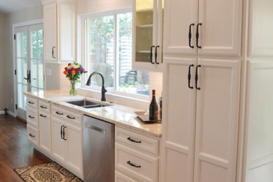 Example of a small transitional galley dark wood floor, brown floor and vaulted ceiling kitchen design in Denver with a double-bowl sink, raised-panel cabinets, white cabinets, granite countertops, white backsplash, subway tile backsplash, stainless steel appliances, a peninsula and beige countertops