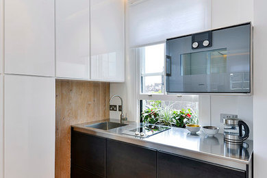This is an example of a small contemporary kitchen in London with a single-bowl sink, stainless steel cabinets, stainless steel benchtops, stainless steel appliances and light hardwood floors.