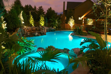 This is an example of a mid-sized country backyard custom-shaped pool in Kansas City with a water feature and natural stone pavers.