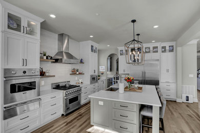 Large transitional l-shaped medium tone wood floor and brown floor open concept kitchen photo in DC Metro with a farmhouse sink, shaker cabinets, white cabinets, quartz countertops, white backsplash, subway tile backsplash, stainless steel appliances, an island and white countertops
