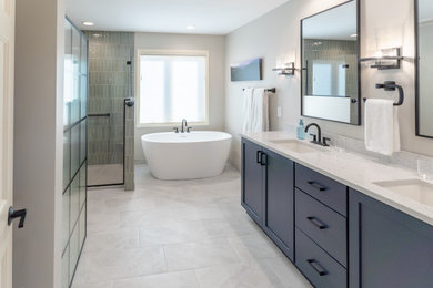 Large traditional ensuite bathroom in Milwaukee with recessed-panel cabinets, blue cabinets, a corner bath, an alcove shower, a two-piece toilet, grey walls, ceramic flooring, a submerged sink, engineered stone worktops, grey floors, a hinged door, white worktops, double sinks and a built in vanity unit.