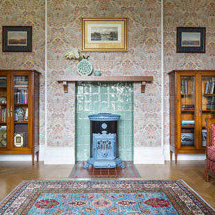 Новый формат декора квартиры: парадная гостиная комната среднего размера в стиле фьюжн с разноцветными стенами, светлым паркетным полом, печью-буржуйкой и фасадом камина из плитки