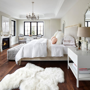 Cette photo montre une chambre parentale chic avec un mur beige, un sol en bois brun, une cheminée standard, un manteau de cheminée en bois et un sol marron.