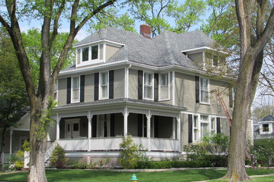This is an example of a large traditional two-storey beige house exterior in Chicago with vinyl siding, a clipped gable roof and a shingle roof.