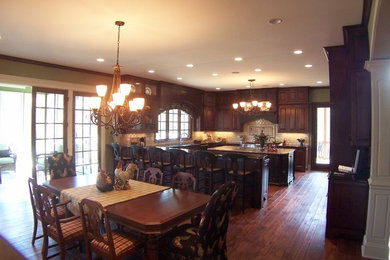 This is an example of a large traditional u-shaped eat-in kitchen in Chicago with an undermount sink, raised-panel cabinets, dark wood cabinets, granite benchtops, beige splashback, ceramic splashback, stainless steel appliances, dark hardwood floors and with island.
