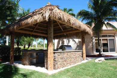 Photo of a large tropical backyard patio in Miami with an outdoor kitchen, natural stone pavers and a gazebo/cabana.