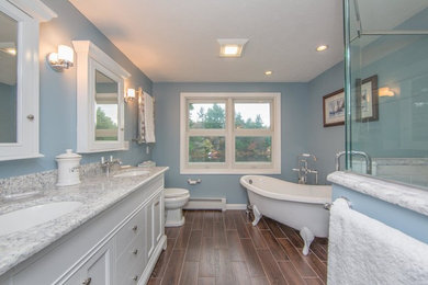 This is an example of a mid-sized traditional master bathroom in Boston with shaker cabinets, white cabinets, a corner shower, a two-piece toilet, blue walls, an undermount sink, granite benchtops, a hinged shower door, gray tile, marble, dark hardwood floors, brown floor, grey benchtops and a claw-foot tub.