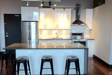 Mid-sized modern single-wall eat-in kitchen in Toronto with a single-bowl sink, flat-panel cabinets, white cabinets, quartz benchtops, white splashback, subway tile splashback, stainless steel appliances, medium hardwood floors and with island.