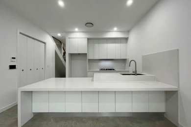 Design ideas for a mid-sized modern galley open plan kitchen in Sydney with an undermount sink, white cabinets, black appliances, ceramic floors, with island and grey floor.