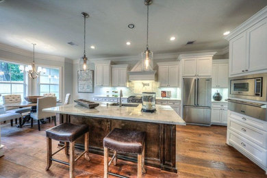 Large transitional medium tone wood floor open concept kitchen photo in Houston with a drop-in sink, shaker cabinets, white cabinets, quartzite countertops, gray backsplash, stone tile backsplash, stainless steel appliances and an island