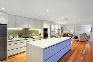 Design ideas for a large modern galley open plan kitchen in Melbourne with a double-bowl sink, flat-panel cabinets, white cabinets, green splashback, glass sheet splashback, stainless steel appliances, medium hardwood floors and with island.