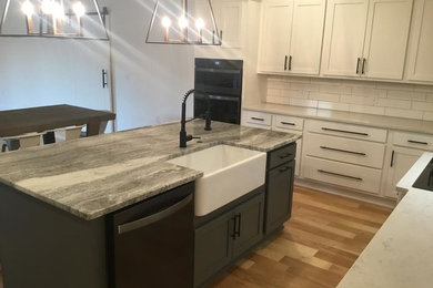 Mid-sized country l-shaped open plan kitchen in Little Rock with a farmhouse sink, shaker cabinets, white cabinets, white splashback, ceramic splashback, stainless steel appliances, medium hardwood floors, with island, brown floor and grey benchtop.