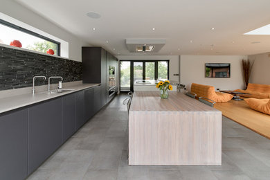 Design ideas for an expansive contemporary single-wall open plan kitchen in Buckinghamshire with a submerged sink, flat-panel cabinets, black cabinets, quartz worktops, black splashback, mosaic tiled splashback, integrated appliances, porcelain flooring, an island and grey floors.