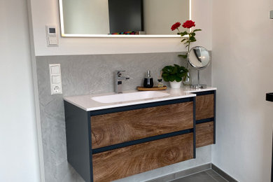 Modernes Badezimmer mit dunklen Holzschränken, grauen Fliesen, Mineralwerkstoff-Waschtisch, weißer Waschtischplatte, Einzelwaschbecken und eingebautem Waschtisch in Stuttgart