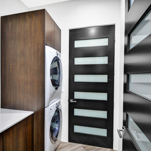 Medium sized contemporary single-wall separated utility room in Los Angeles with flat-panel cabinets, medium wood cabinets, glass worktops, white walls, porcelain flooring and a stacked washer and dryer.