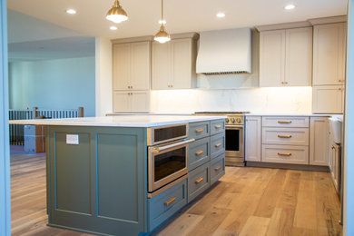 Inspiration for a large modern l-shaped medium tone wood floor open concept kitchen remodel in Indianapolis with a farmhouse sink, recessed-panel cabinets, beige cabinets, marble countertops, white backsplash, marble backsplash, stainless steel appliances, an island and white countertops