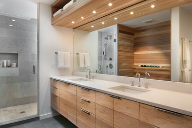 This is an example of a contemporary bathroom in DC Metro with flat-panel cabinets, medium wood cabinets, an alcove shower, gray tile, white walls, an undermount sink, grey floor, a hinged shower door and white benchtops.