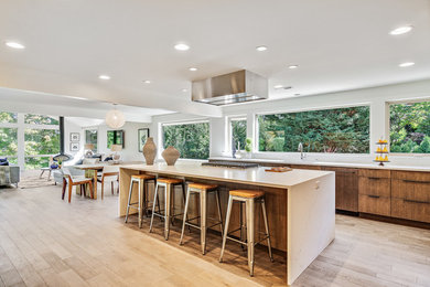 Design ideas for a midcentury galley open plan kitchen in Seattle with flat-panel cabinets, medium wood cabinets, white splashback, panelled appliances, light hardwood floors, with island, beige floor and white benchtop.