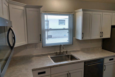 Mid-sized trendy l-shaped linoleum floor and brown floor kitchen pantry photo in Other with a drop-in sink, recessed-panel cabinets, white cabinets, laminate countertops, white backsplash, subway tile backsplash, stainless steel appliances, no island and gray countertops