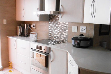 Small elegant u-shaped porcelain tile eat-in kitchen photo in Other with a double-bowl sink, shaker cabinets, white cabinets, granite countertops, gray backsplash, mosaic tile backsplash, stainless steel appliances and no island