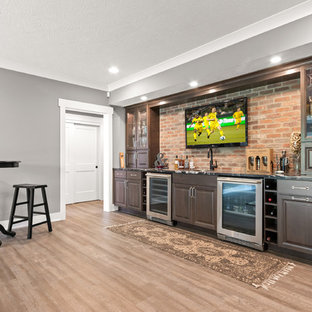 コロンバスの中サイズのおしゃれなウェットバー (アンダーカウンターシンク、レイズドパネル扉のキャビネット、濃色木目調キャビネット、オニキスカウンター、赤いキッチンパネル、レンガのキッチンパネル、クッションフロア、ベージュの床、黒いキッチンカウンター) の写真