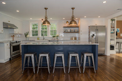 Photo of a mid-sized country l-shaped eat-in kitchen in Boston with a farmhouse sink, shaker cabinets, white cabinets, quartzite benchtops, white splashback, subway tile splashback, stainless steel appliances, medium hardwood floors, with island, brown floor and white benchtop.