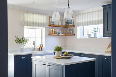 Design ideas for a medium sized coastal u-shaped enclosed kitchen in Hampshire with a belfast sink, shaker cabinets, blue cabinets, granite worktops, ceramic splashback, black appliances, laminate floors, an island and white worktops.