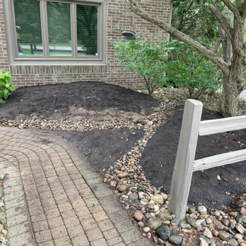 River rock drain channel beside a brick paver walkway