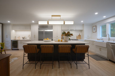 Inspiration for a 1960s l-shaped light wood floor and brown floor eat-in kitchen remodel in Boston with a farmhouse sink, shaker cabinets, white cabinets, quartz countertops, white backsplash, quartz backsplash, stainless steel appliances, an island and white countertops