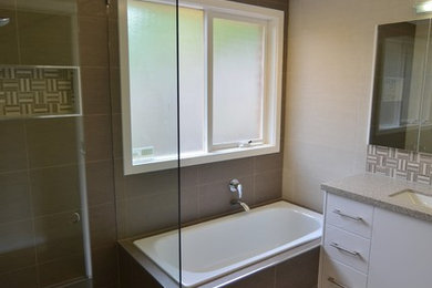 Photo of a mid-sized modern kids bathroom in Melbourne with an undermount sink, open cabinets, white cabinets, granite benchtops, a drop-in tub, a corner shower, gray tile, ceramic tile, beige walls and ceramic floors.